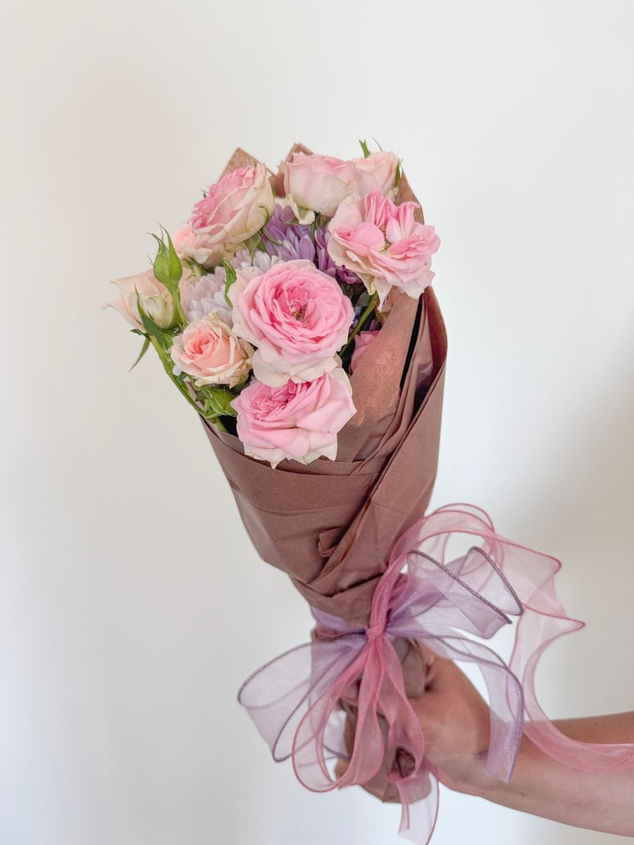 Soft pink roses and lilac chrysanthemums wrapped in rose-brown paper with a sheer ribbon