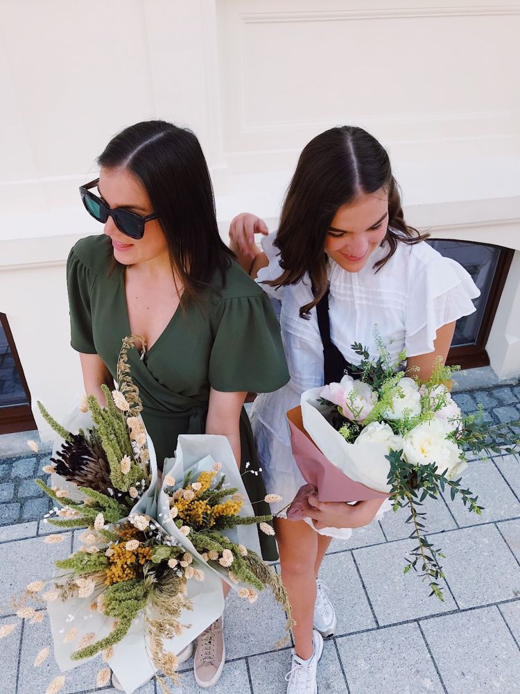 Two friends holding a dried-flower bouquet and a pink-wrapped peony bouquet