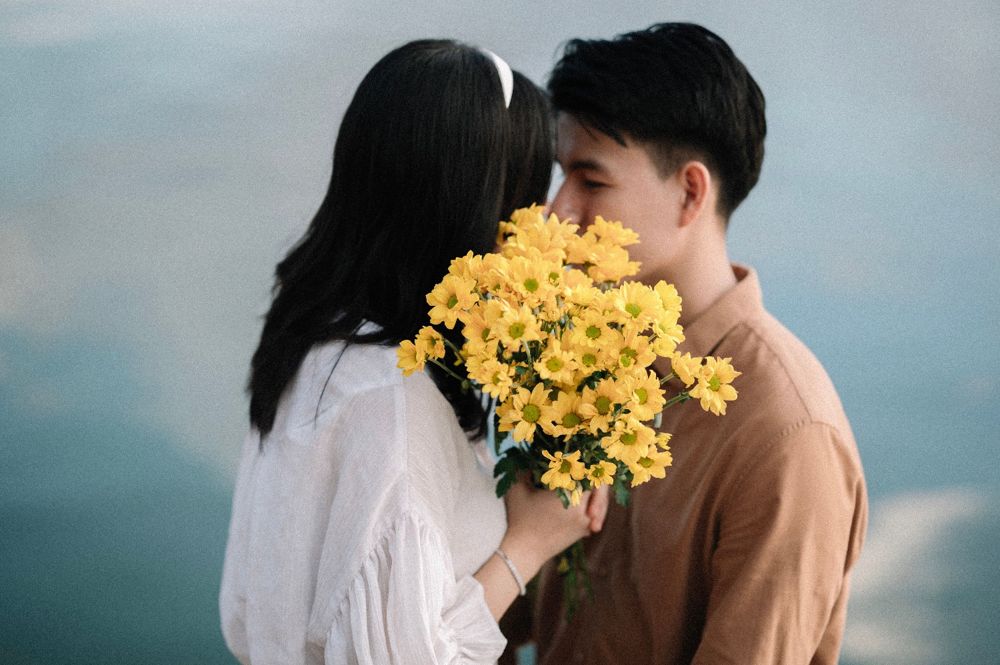 A couple behind a big bunch of yellow daisies