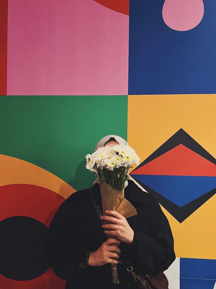 Someone holding white chrysanthemums in kraft paper against a colourful mural